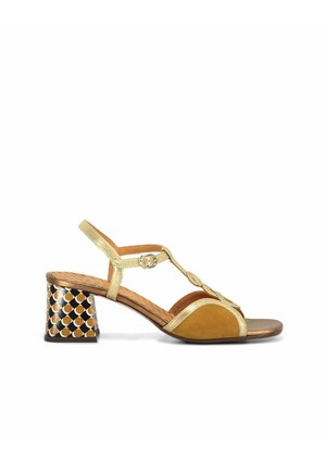 Sandale à talon femme avec des brides dorées, devant en daim marron et talon bloc imprimé avec un motif géométrique noir, marron et blanc.