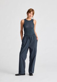 Top senza maniche di un verde bluastro scuro abbinato a pantaloni blu navy a vestibilità ampia e scarpe nero piatte. Il top ha un design aderente, i pantaloni presentano una vita elastica.