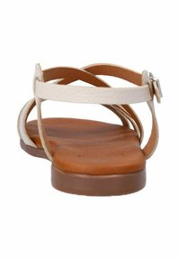 Strappy sandals with a light beige leather upper, featuring a flat brown sole. Adjustable ankle strap with a silver buckle.
