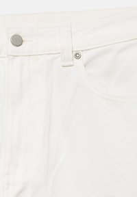 Gros plan de la ceinture d'un jean en denim blanc montrant un bouton en métal, une boucle de ceinture, et le bord de la poche avant avec rivet.
