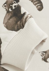 Lichtgekleurde sweatshirtmanchet met een geribbelde textuur, versierd met een subtiel wasberenpatroon in donkerbruin en grijstinten.