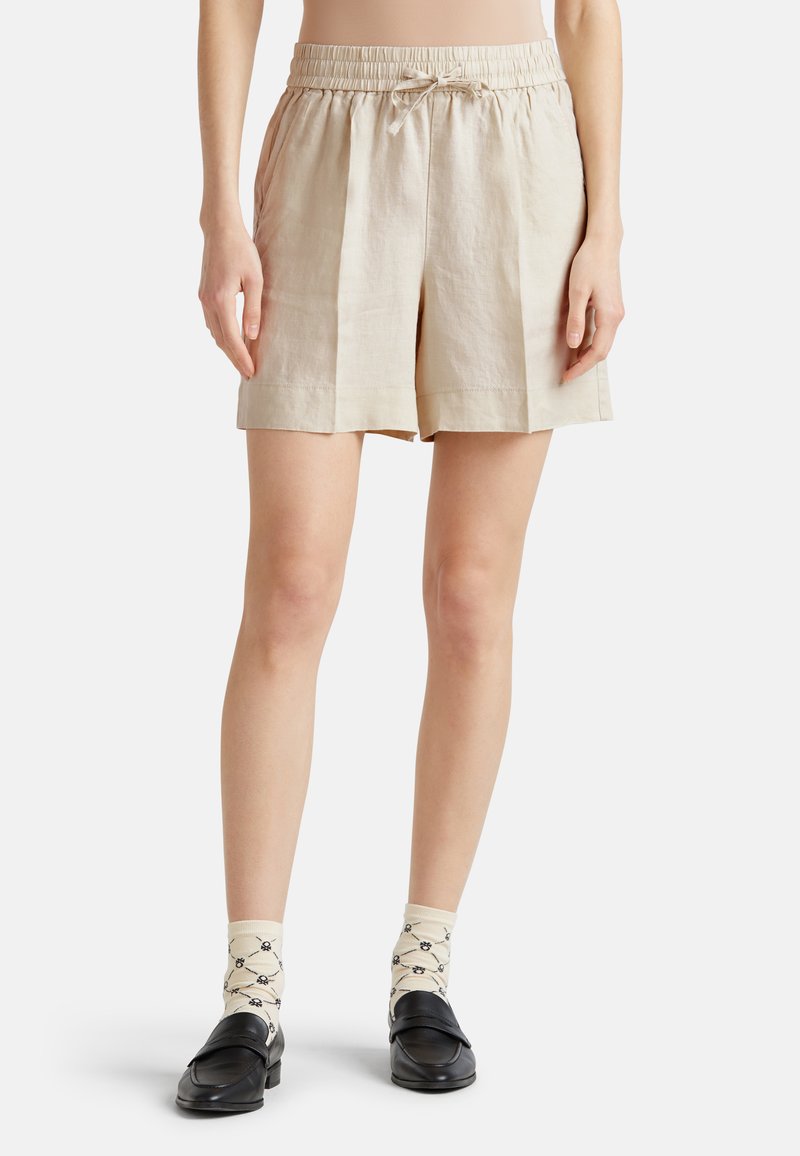Shorts en lin beige avec une taille élastique et un cordon de serrage, dotés de poches latérales et d'une coupe décontractée. Associés à des chaussettes crème à motifs et des chaussures noires.