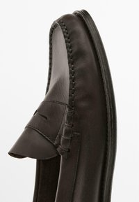 Black leather loafers featuring stitched detailing, a flat heel, and a smooth texture. The design includes a decorative vamp accent.