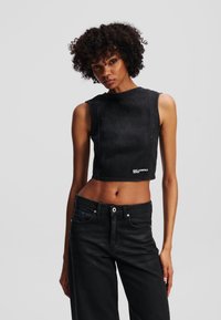 Top scurt din denim negru cu design fără mâneci, având un decolteu rotund și detalii de cusătură vizibile, asortat cu blugi negri cu talie înaltă.