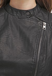 Zwarte leren jas met een hoge kraag, diagonale rits en drukknoopdetail. Heeft een gestructureerde afwerking en zichtbare stiksels.