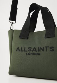 Zöld vászontáska fekete részletekkel, amelyen a "ALLSAINTS LONDON" felirat szerepel kiemelkedő fekete betűkkel. Két felső fogantyúval és levehető pánttal rendelkezik.