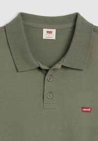 Polo de culoare verde măslin cu o croială standard, având un guler ribetat, placket cu trei nasturi și logo-ul roșu Levi's pe pieptul stâng.