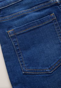 Tissu en denim bleu avec une poche arrière cousue et des coutures visibles de fil orange sur un jean.