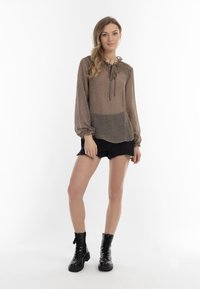 Lett, gennemsigtig beige bluse med tekstureret mønster, samlet halsudskæring og elastiske manchetter. Sammen med sorte denimshorts og sorte kampstøvler.