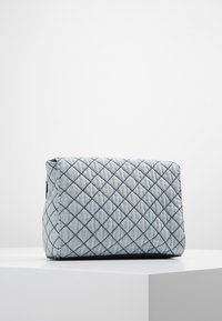 Borsa in tessuto trapuntato blu chiaro con cuciture a diamante, in posizione verticale su un piedistallo bianco contro uno sfondo semplice.