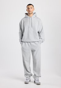 Ensemble sweat à capuche gris avec pantalon assorti, fabriqué en tissu doux. Le sweat à capuche comprend une poche kangourou et un cordon de serrage, le pantalon possède des poignets élastiques.