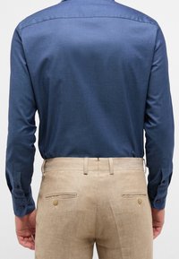 Dark blue long-sleeve shirt with a smooth texture, paired with beige trousers featuring a textured fabric and two back pockets with buttons.