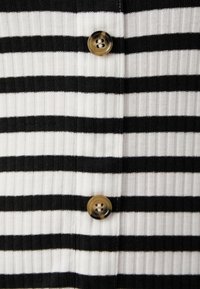Tissu côtelé rayé noir et blanc avec trois boutons ronds, deux dans une teinte foncée et un dans un design marbré clair.