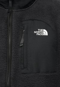 Μαύρο φλίς τζάκετ με φερμουάρ και τσέπη στο στήθος που φέρει το λογότυπο The North Face σε λευκό χρώμα.