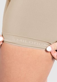 Beige hoge taille slip van een gladde, geribbelde stof. Kenmerkt zich door een subtiele reliëflogo op de tailleband en een nauwsluitend ontwerp.