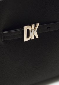 Black textured leather handbag with a slim strap and shiny metallic DKNY logo buckle on the front.
