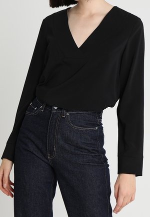 Zwarte blouse met lange mouwen en een V-halsontwerp, gemaakt van gladde stof. Gecombineerd met donkerblauwe, hoogtaillespijkerbroek met klassieke stiksels.