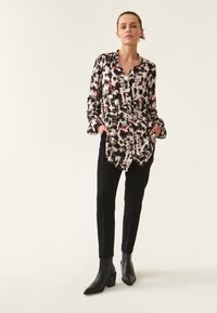 Blusa de manga larga en un patrón abstracto en negro, blanco y rojo, hecha de una tela ligera, combinada con pantalones negros de corte ajustado y botas de tobillo.