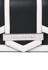 Sac à main noir en cuir avec des accents blancs, une forme structurée et une plaque en métal argenté portant la gravure "KARL LAGERFELD".