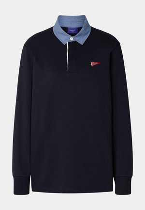 Czarna koszulka polo z długim rękawem, niebieskim kołnierzem chambray, pojedynczym białym guzikiem i małym czerwonym trójkątnym logo na lewej piersi.