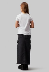 Wit shirt met korte mouwen gecombineerd met een lange zwarte spijkerrok met cargozakken en een rechte snit, gedragen met zwarte plateau schoenen.