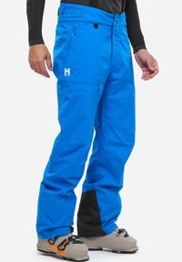 Blaue Skihosen aus wasserabweisendem Material, mit Reißverschlusstaschen, einem Logo am Oberschenkel und einem schwarzen Akzent an den Bündchen.