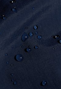 Vodna kapljica se zbira na temno modri vodoodporni tkanini, kar poudarja teksturo in vodoodpornost materiala.