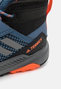 Niebiesko-czarny but trekkingowy z siateczkową cholewką, odblaskowymi akcentami, teksturowaną podeszwą i pomarańczowymi detalami; wyróżnia się marką Adidas Terrex.