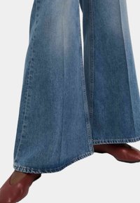 Jeans z wysokim stanem i szerokimi nogawkami w jasnoniebieskim dżinsie z wyblakłymi częściami i kontrastowymi szwami. Połączone z bordowymi butami na końcówkach w szpic.