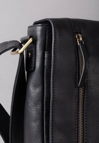Black leather bag with a textured surface, featuring a gold zipper, metal hardware, and a detachable strap. Rectangular shape with rounded edges.