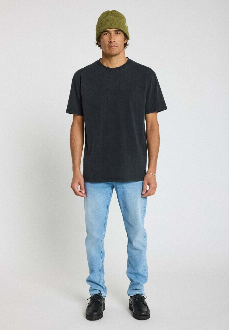 T-shirt en coton noir, coupe régulière, avec col rond. Jean bleu clair, jambe droite, en denim. Chaussures noires à lacets et bonnet en tricot vert.