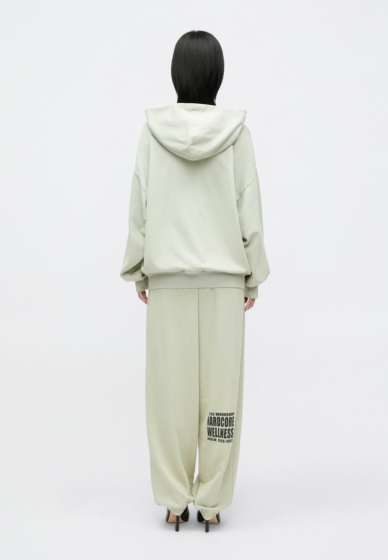 Lichtgroene hoodie met een capuchon, ruime pasvorm en een voorzak; gecombineerd met bijpassende wijde broek met een gedrukt logo op het been.