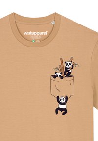 Beige Baumwoll-T-Shirt mit verspielten Panda-Grafiken, Bambusstäben und einem Taschendesign auf der Vorderseite, mit Akzenten in Schwarz und Weiß.