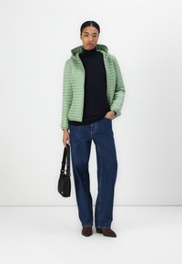 Lys grøn pufferjakke med høj krave, quiltet tekstur, parret med en mørk turtleneck og brede denimbukser i blå. Sorte taskeaccenter.