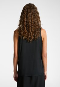 Top senza maniche nero con una texture liscia, leggermente morbido e orlo arrotondato, che mette in mostra un design minimalista.