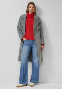 Szary wełniany płaszcz z dwurzędowym zapięciem, czerwony dziany golf, szerokie niebieskie dżinsy oraz kremowe trampki z brązowymi podeszwami.