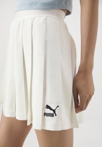 Witte plissérok met een gladde textuur, voorzien van het PUMA-logo in zwarte borduursels vlak bij de zoom. Eenvoudig ontwerp met een aansluitende tailleband.