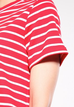 Chemise à manches courtes à rayures horizontales rouges et blanches portée sur le haut du bras et l'épaule d'une personne sur fond blanc.