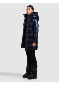 Nāvijas pūdera jaka ar kapuci, spīdīgu virsmu, horizontālu šuvumu un priekšēju rāvējslēdzēju. Valda kopā ar melniem, mežģīņu stiprinājuma, izolētiem sniega zābakiem.