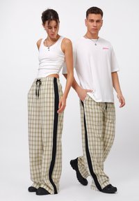 Bred og svart rutete bukser med strikk i livet, sidelister og avslappet passform; kombinert med en hvit tank top og t-skjorte.