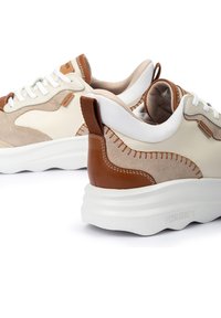 Une paire de baskets en suède beige et brun avec des lacets blancs et de épaisses semelles blanches sur un fond blanc.