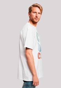 White cotton t-shirt featuring multi-colored graphics on the front, short sleeves, and a loose fit, paired with blue denim jeans.