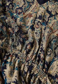 Tissu avec des motifs floraux et cachemire complexes en bleu, beige et rouge, avec un détail élastique froncé et de subtils accents dorés.