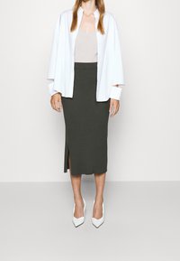 White oversized shirt, beige top, dark green ribbed midi skirt with a side slit, and white pointed-toe high heels.
