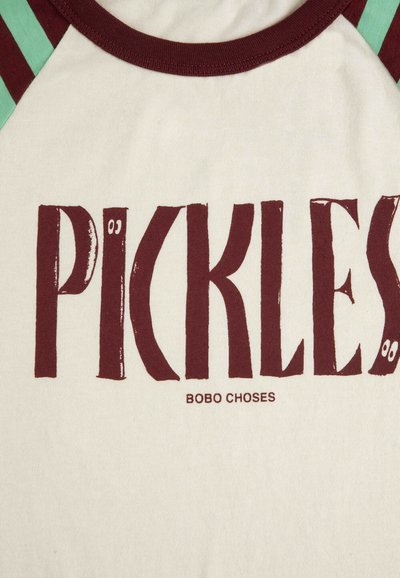 Maglietta bianca e marrone con la scritta marrone "PICKLES" caratterizzata da piccoli occhi su due lettere e "BOBO CHOSES" stampato sotto.