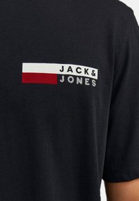 Schwarzes T-Shirt aus Baumwolle mit einem Frontdruck, der den Text "JACK & JONES" sowie horizontale Streifen in Rot und Weiß zeigt. Angenehme Textur.