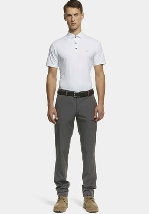 Witte poloshirt met een kraag en drie knopen, gecombineerd met grijze broek met zakken en een zwarte geweven riem. Bruine schoenen maken de outfit af.
