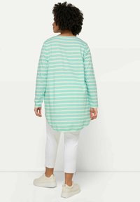 Lång, mintgrön randig topp med vita ränder, med rundad nederkant. I kombination med vita capribyxor och ljusa sneakers.