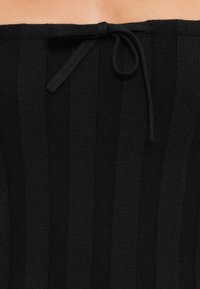 Material negru, cu o textură în dungi verticale și un detaliu cu bretele la talie. Textura este netedă, cu un design care se potriveste strâns.