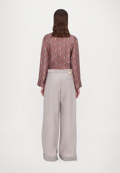 Långärmad blus i mauve med geometriskt tryck; vida ljusgrå byxor med elastisk midja och liten logotypetikett på baksidan.